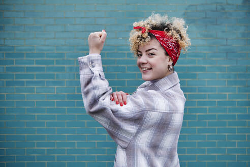 Smiling curly haired woman in bandana flexing muscles - ASGF00072