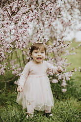 Baby Mädchen spielt mit Blumen von Kirschbaum im Frühling - GMLF01077