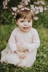 Baby girl sitting on grass near cherry tree in springtime - GMLF01078