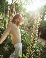 Side view of tranquil female standing in green summer garden on sunny day and looking down - ADSF21269