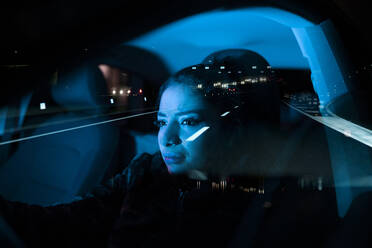 Spiegelung in der Windschutzscheibe einer frustrierten Autofahrerin, die weint, während sie in einem auf nächtlicher Fahrbahn geparkten Auto sitzt - ADSF21337