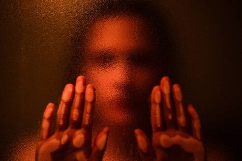 Anonymous blurred female touching glass while standing in dark room with orange illumination - ADSF21344