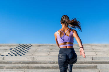 Low angle back view of unrecognizable fit female in activewear running up stone staircase in city during dynamic cardio training - ADSF21365