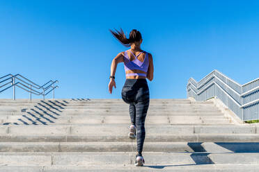 Low angle back view of unrecognizable fit female in activewear running up stone staircase in city during dynamic cardio training - ADSF21366