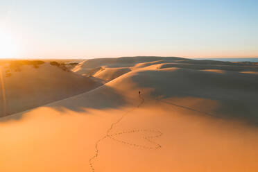 Von oben entfernt unerkennbar Reisenden zu Fuß auf malerischen Sanddünen in der Nähe von Ozean gegen wolkenlosen Sonnenuntergang Himmel in Australien - ADSF21391