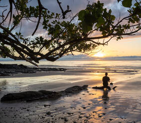 Rückenansicht der Silhouette eines Mannes, der sich am nassen Strand entspannt und den spektakulären Sonnenuntergang über dem Meer in Australien bewundert - ADSF21424