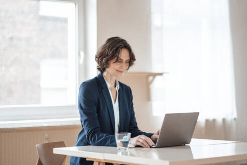 Reife Geschäftsfrau mit Laptop auf dem Tisch im Heimbüro - MOEF03654