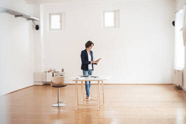 Geschäftsfrau mit digitalem Tablet vor weißer Wand im Heimbüro - MOEF03660
