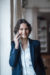 Lächelnde Geschäftsfrau, die zu Hause mit ihrem Smartphone telefoniert - MOEF03667