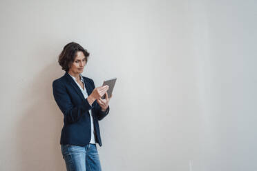 Frau benutzt digitales Tablet und lehnt sich an eine weiße Wand - MOEF03670