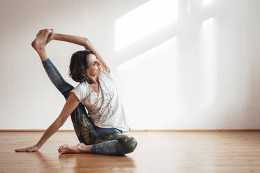 Frau übt Yoga vor einer weißen Wand in einem Gesundheitsstudio - MOEF03685