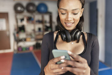 Lächelnde junge Frau, die im Fitnessstudio ein Mobiltelefon benutzt - JPTF00715