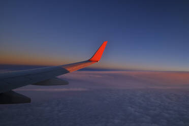 Wing of commercial airplane flying against sky at dusk - RUEF03240