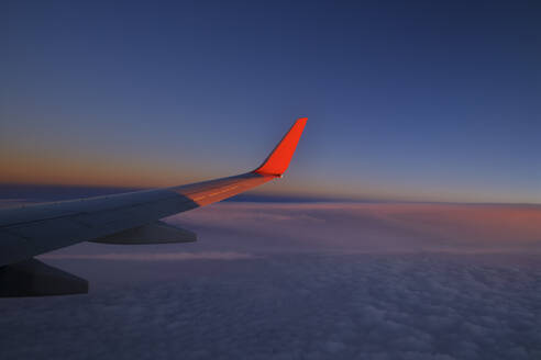 Flügel eines Verkehrsflugzeugs fliegen gegen den Himmel in der Abenddämmerung - RUEF03240