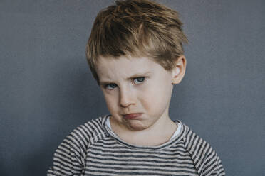 Innocent boy making face on gray background - MFF07617