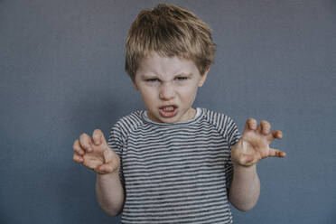 Angry boy gesturing while standing against gray background - MFF07619