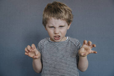 Wütender Junge gestikuliert im Stehen vor grauem Hintergrund - MFF07619