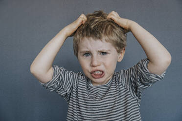 Frustrated boy scratching head against gray background - MFF07620