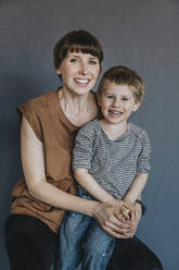 Mother and son sitting against gray background - MFF07623