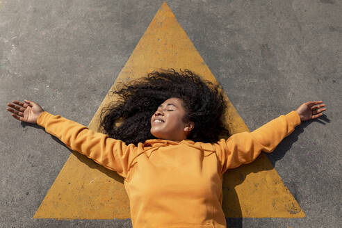 Carefree young woman with eyes closed lying down on footpath - TCEF01658