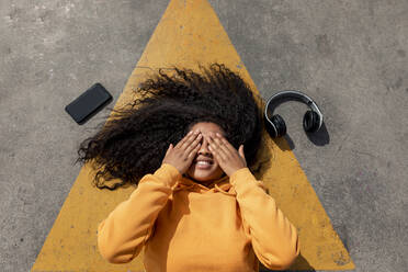 Young woman covering eyes while lying down on footpath - TCEF01659
