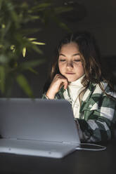 Mädchen mit braunem Haar studiert durch digitale Tablet am Tisch in der Wohnung - JAQF00368