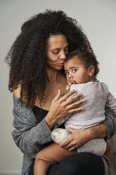 Curly haired woman carrying daughter on gray background - AKLF00131