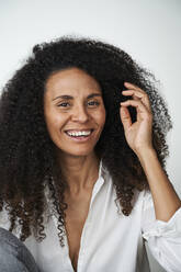 Happy woman with hand in hair over gray background - AKLF00136
