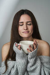 Woman with eyes closed holding cup of tea on gray background - AKLF00149