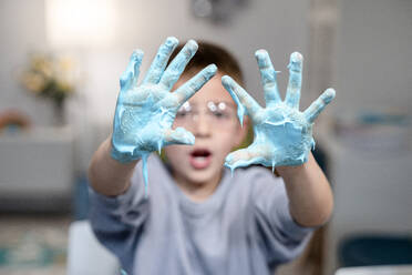 Junge zeigt Hände mit blauer schleimiger Flüssigkeit zu Hause - AMPF00113