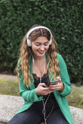 Smiling woman using mobile phone while listening music through headphones - JRVF00364