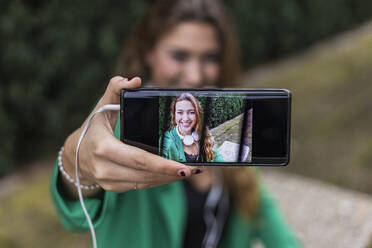 Frau zeigt mit Smartphone aufgenommenes Selfie im Freien - JRVF00367