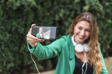 Lächelnde Frau, die im Park ein Selfie mit ihrem Smartphone macht - JRVF00368