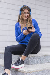 Smiling woman listening music through headphones while sitting on steps - JRVF00374