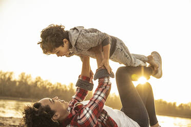 Playful mother picking up son while playing during sunset - UUF22982