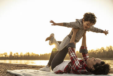 Young woman picking up boy with arms outstretched while playing during sunset - UUF22983