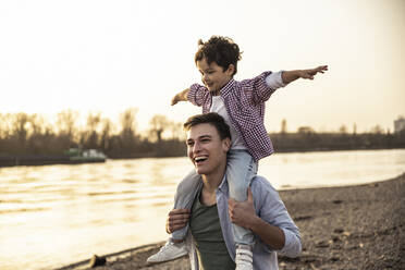 Smiling man playful boy on shoulders by lake - UUF22990