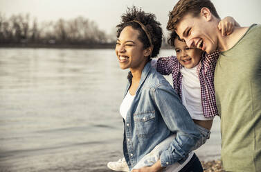 Cheerful family standing by lake during sunset - UUF22999