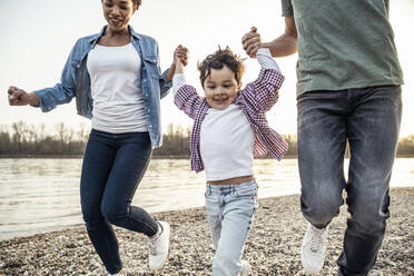 Verspielte Familie, die sich beim Laufen am See an den Händen hält - UUF23009