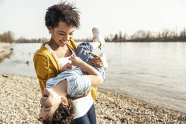 Playful mother carrying son while playing by lake - UUF23018