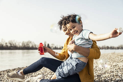 Playful mother and son playing with bubble soap on sunny day - UUF23030