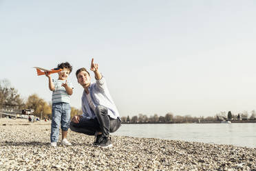 Father gesturing while crouching by son standing with toy on sunny day - UUF23042