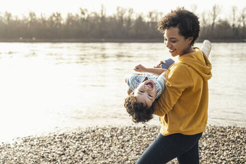 Lächelnde Mutter mit fröhlichem Jungen auf dem Arm am See - UUF23051