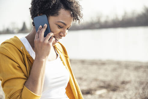 Lächelnde Frau, die an einem sonnigen Tag im Freien mit einem Mobiltelefon spricht - UUF23070