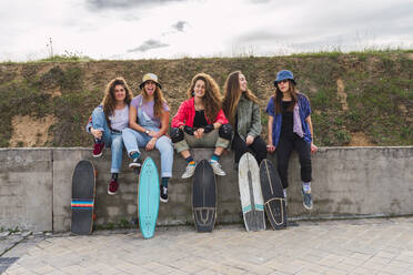 Fröhliche Freundinnen mit Skateboards auf einer Stützmauer sitzend - RSGF00592