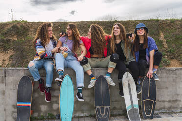 Fröhliche Freundinnen haben Spaß, während sie auf einer Stützmauer sitzen - RSGF00593