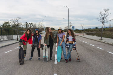 Fröhliche Freundinnen mit Skateboards stehen auf der Straße gegen den Himmel - RSGF00599