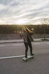Cheerful woman showing horn sign on skateboard - RSGF00612