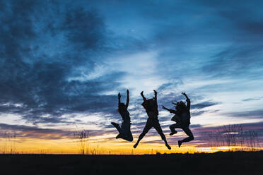 Carefree female friends with arms raised jumping in front of sky - RSGF00615