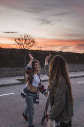 Smiling female friends doing high-five on road during weekend - RSGF00622